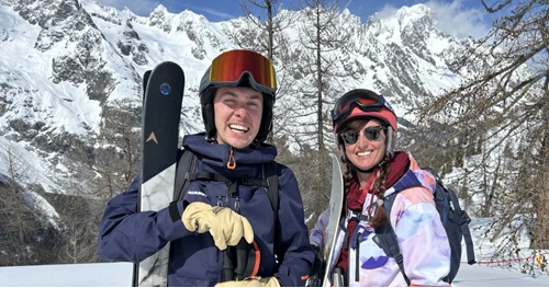Sam and Fleur, winter seasonaires at Action Outdoors posing on the ski slopes with skis and a snowboard.